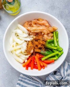 Process shot: A bowl with sliced bell peppers, onion, chicken strips, olive oil, and taco seasoning, all mixed well to coat the ingredients.