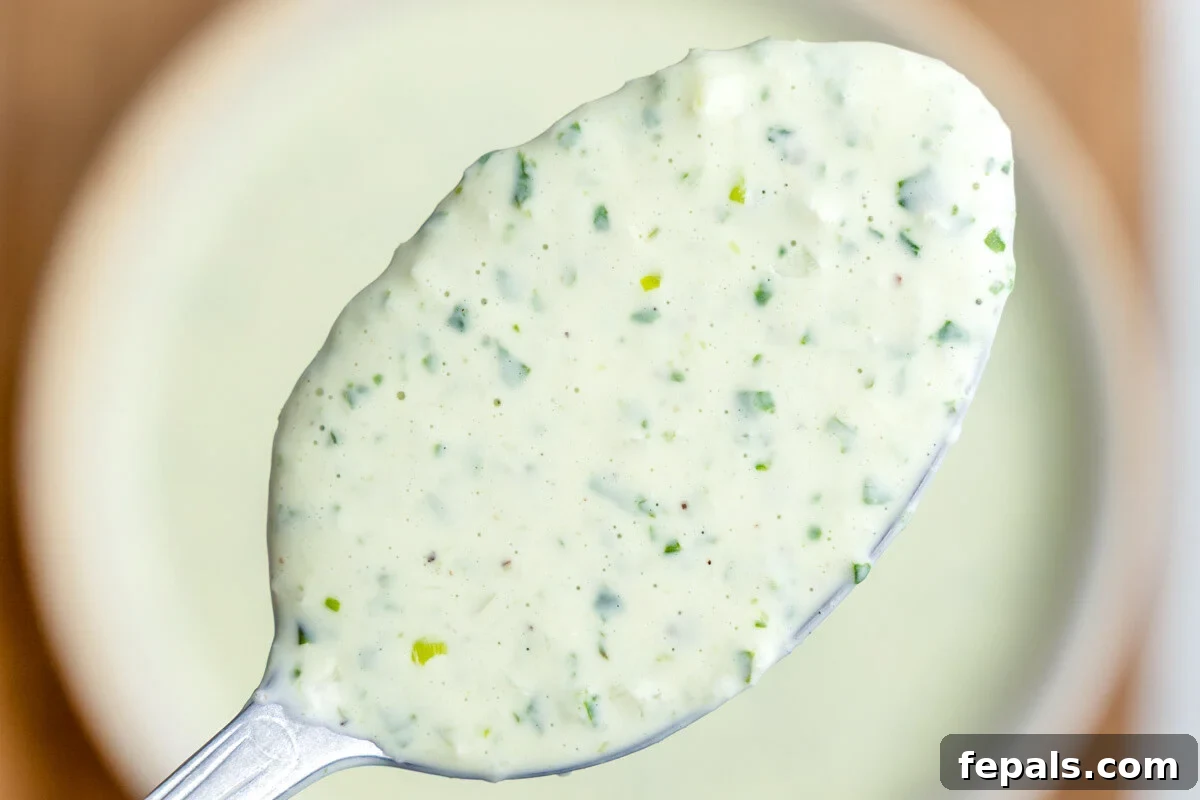 A closeup of a spoonful of green goddess dressing hovering over a bowl.