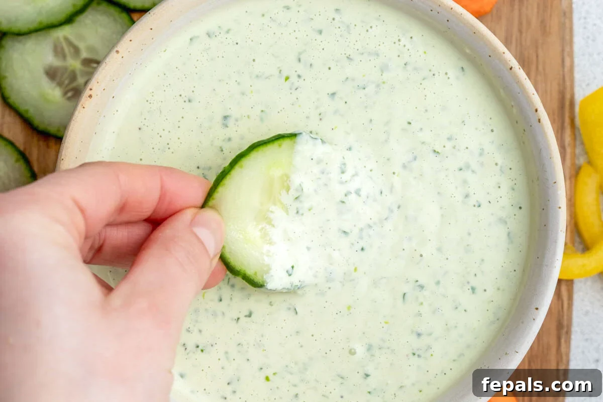 hand holding a slice of cucumber and dipping it in the dressing.