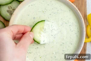 hand holding a slice of cucumber and dipping it in the dressing.