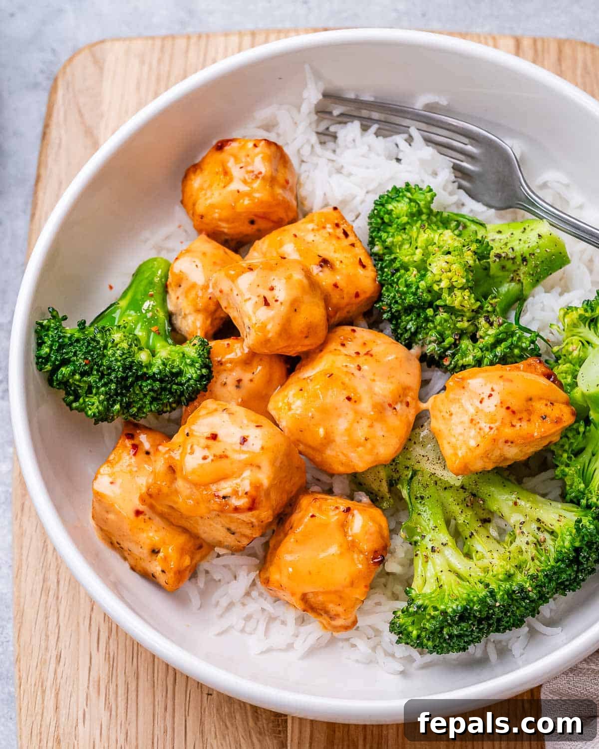 A white bowl with rice, bang bang salmon and broccoli.