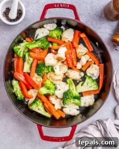 Top view of a red pan with cauliflower, broccoli, and red pepper being browned.