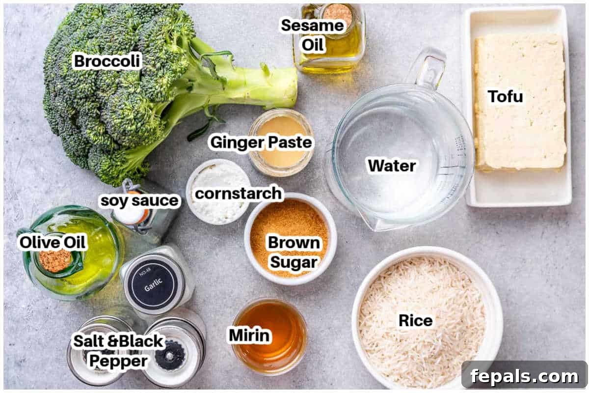 No-Fuss Teriyaki Tofu 3 A flat lay image displaying the key ingredients for making teriyaki tofu, including a block of tofu, fresh broccoli, bottles of soy sauce and mirin, ginger paste, and garlic cloves.
