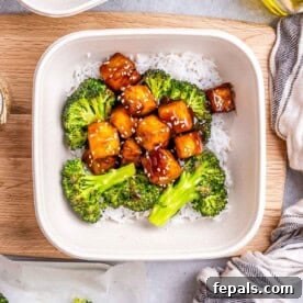 A meal prep bowl with fluffy white rice topped with crispy teriyaki tofu bites and roasted broccoli florets, garnished for a balanced and healthy meal.