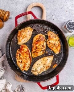 Chicken breasts searing in a large black cast-iron skillet, getting golden-brown.