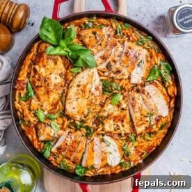 A red skillet with tomato based orzo topped with seared sliced chicken.
