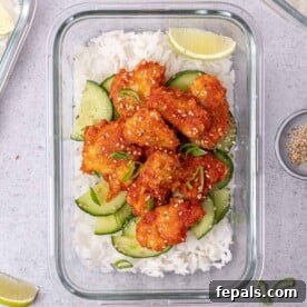 Top-down view of a delicious honey sriracha chicken meal prep bowl, with chicken, white rice, and a refreshing cucumber salad in a glass container.