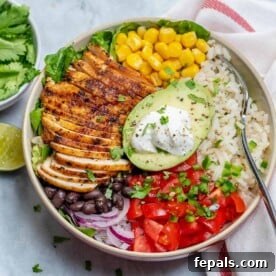 Top-down view of a vibrant chicken burrito bowl, loaded with savory grilled chicken, rice, black beans, corn, diced tomatoes, and a creamy half avocado as the centerpiece.