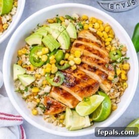 Top view of a vibrant Chipotle chicken rice bowl, showcasing cauliflower rice topped with tender sliced grilled chicken breast, sweet corn, creamy avocado, and sliced jalapeño for a kick.