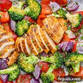 Top view of perfectly sliced chicken breast on a sheet pan, surrounded by beautifully roasted broccoli, onions, and red peppers.