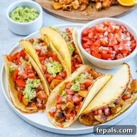 Fully assembled chicken street tacos, bursting with diced chicken, fresh salsa, and creamy guacamole, elegantly presented on a white plate.