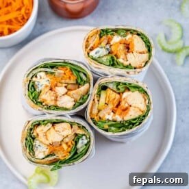 Halved Buffalo grilled chicken sandwich wraps, showcasing their delicious filling, served on a pristine white round plate.