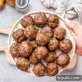 A hand holding a white round plate filled with perfectly browned air fryer meatballs, ready to be served.