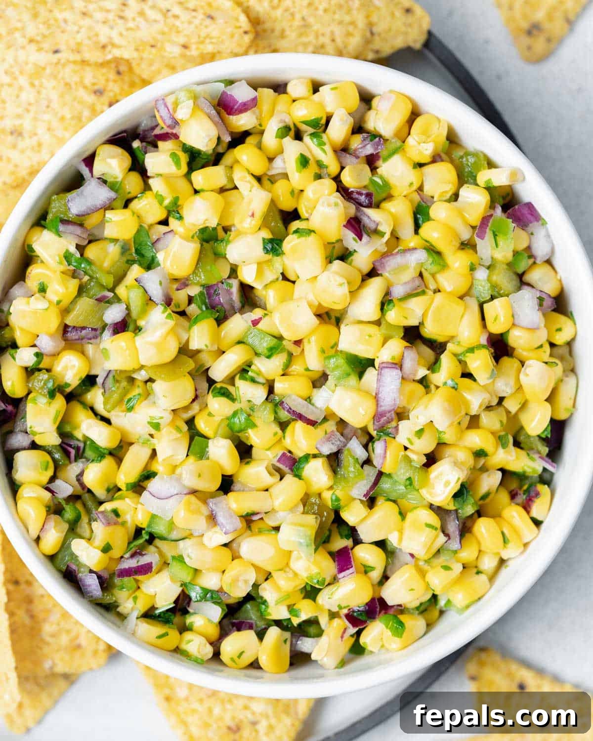 A white bowl of copycat chipotle corn salsa and corn chips, ready to be enjoyed.