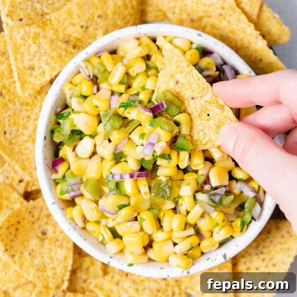 A hand reaching for a tortilla chip loaded with fresh corn salsa.