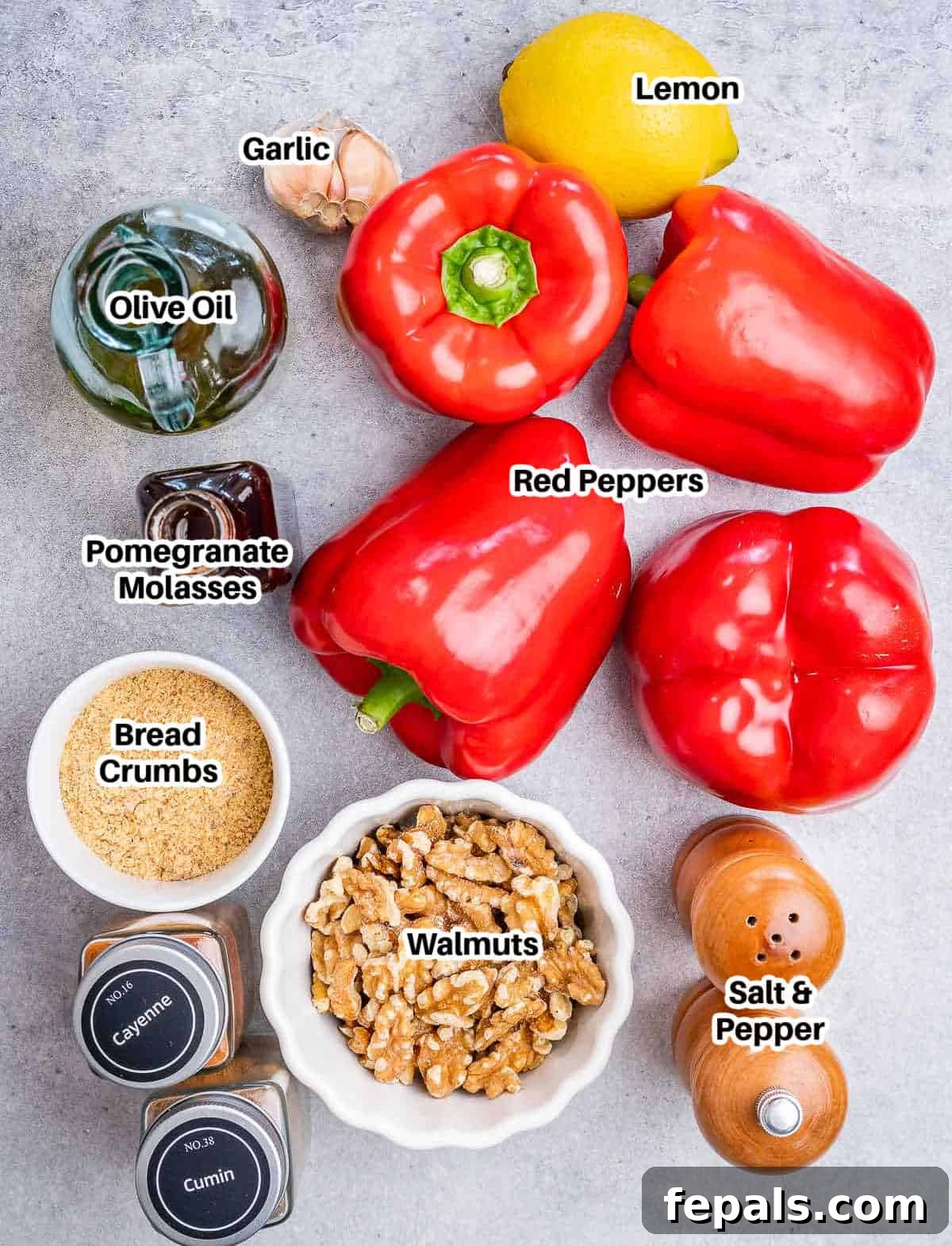 A flat lay image displaying all the fresh and whole ingredients for homemade muhammara, including red bell peppers, walnuts, garlic, breadcrumbs, and a bottle of pomegranate molasses.