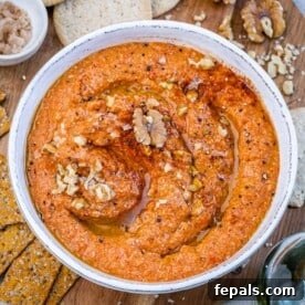 A round bowl of roasted pepper dip called muhammara, garnished with herbs and olive oil.