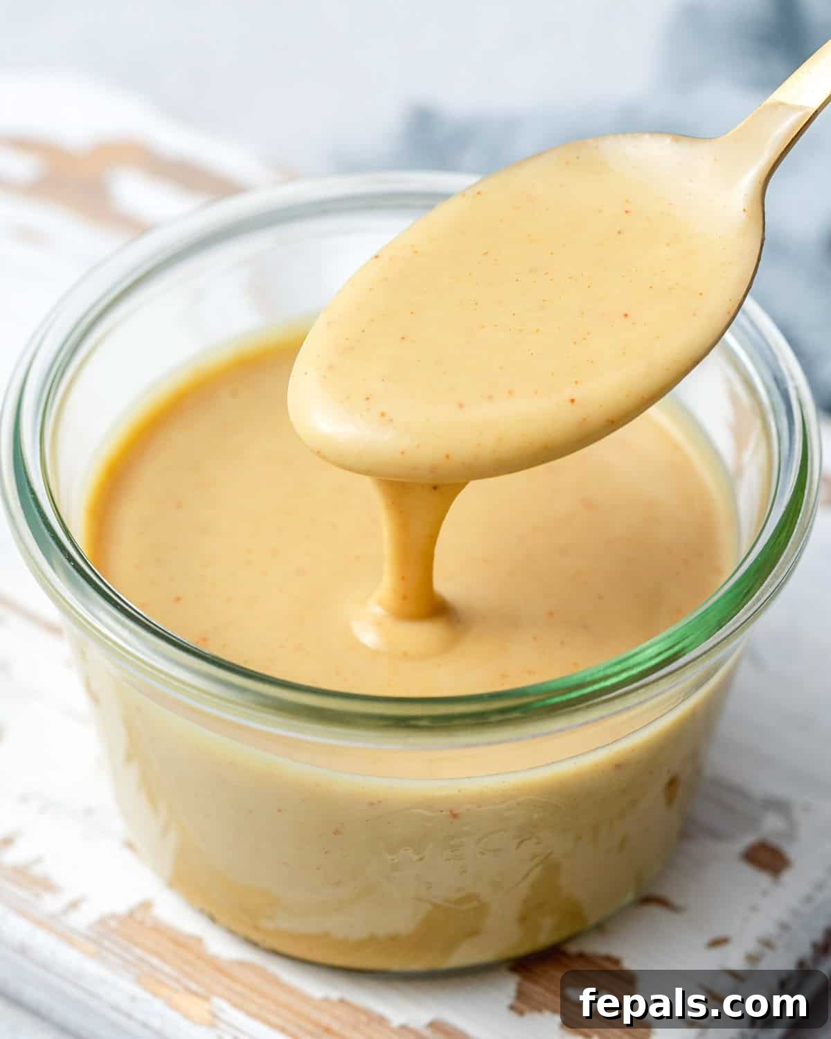 Honey mustard sauce in a jar, with spoon dipped into the sauce, showcasing its creamy texture.