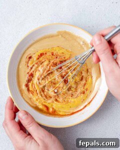 Hand whisks the honey mustard sauce in a bowl.