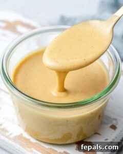 Honey mustard sauce in a jar, with spoon dipped into the sauce, ready for storage.
