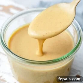 A jar with honey mustard dipping sauce with a spoonful in the jar.