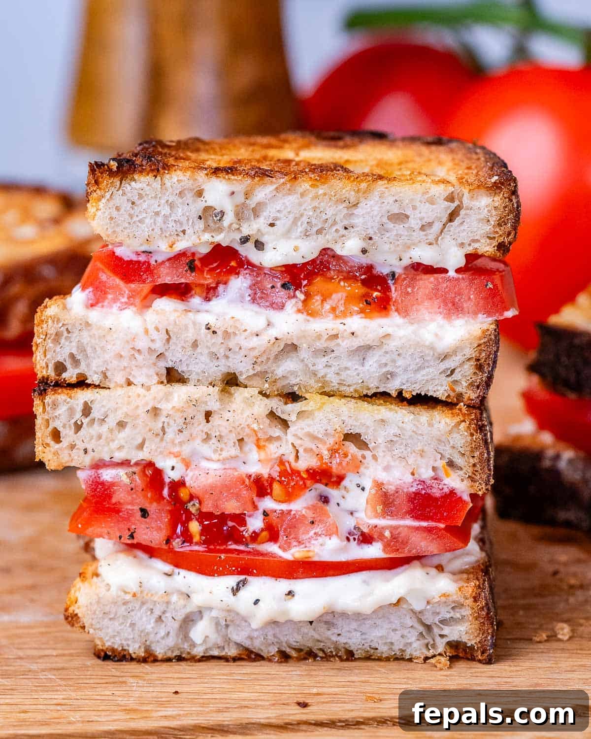 A perfectly assembled tomato sandwich, sliced in half to reveal layers of juicy tomato and creamy spread.