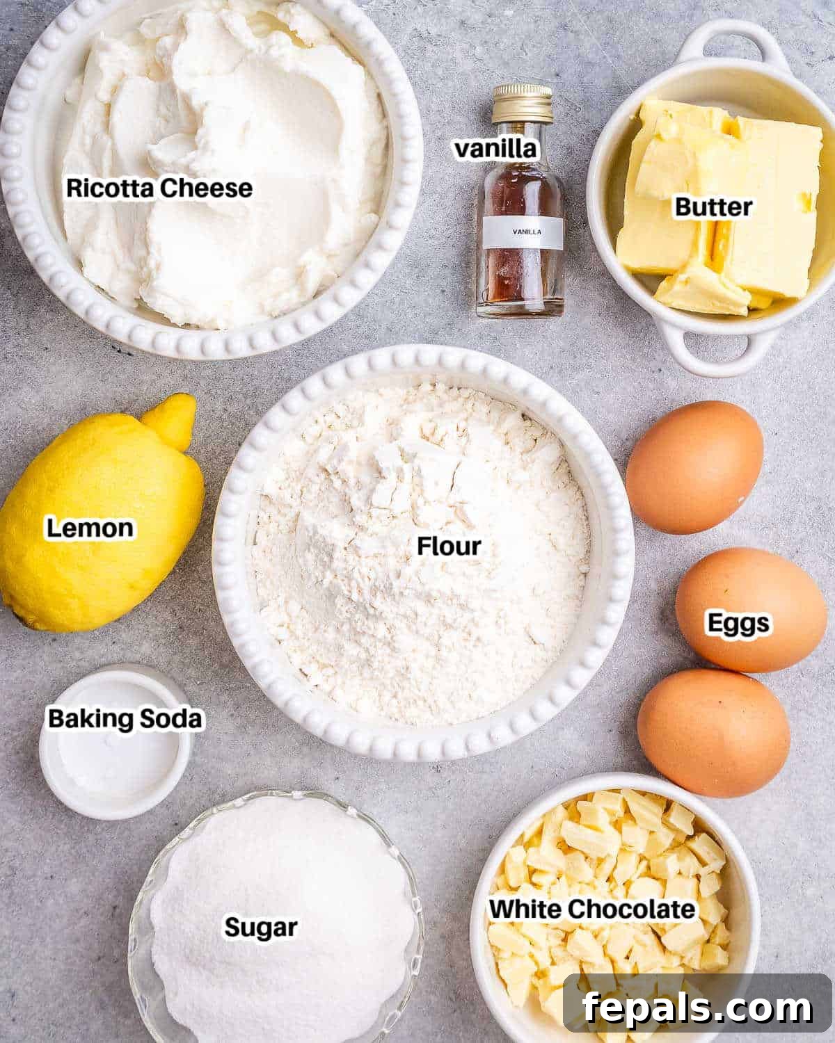 A flat lay photograph displaying all the fresh ingredients needed to bake a lemon ricotta cake, including lemons, eggs, butter, and ricotta cheese.