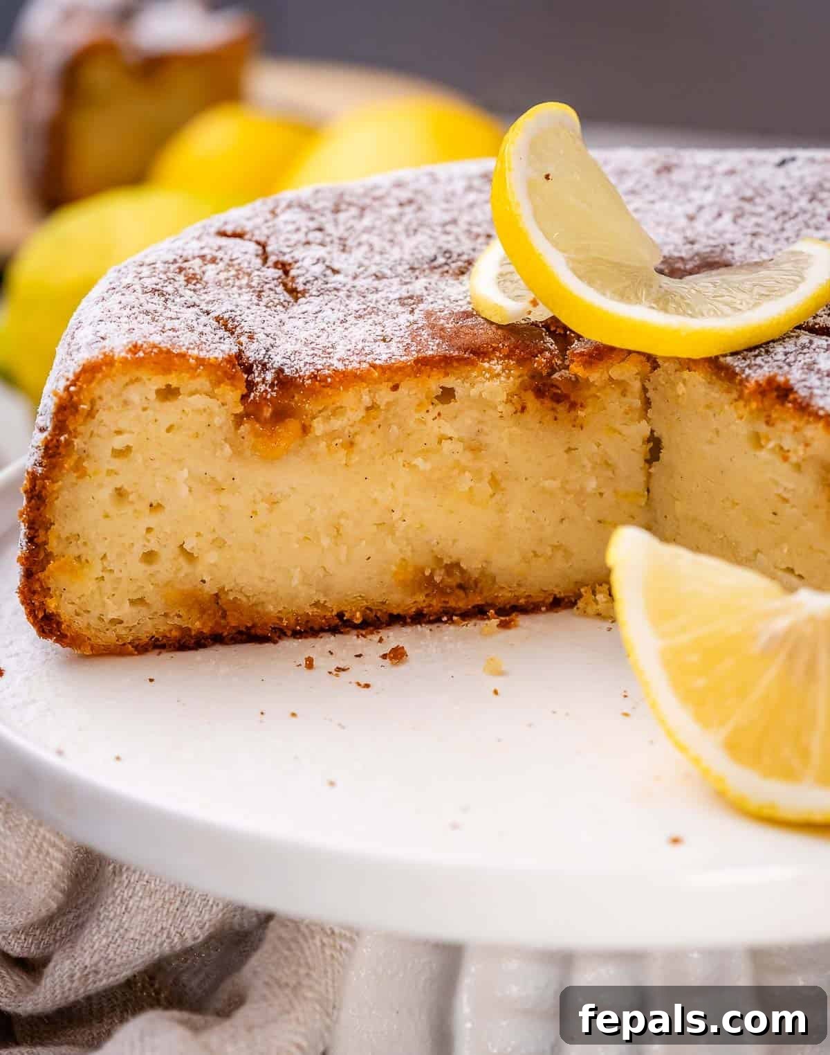 A beautifully presented lemon ricotta cake on a cake pedestal, with several slices ready to be served.