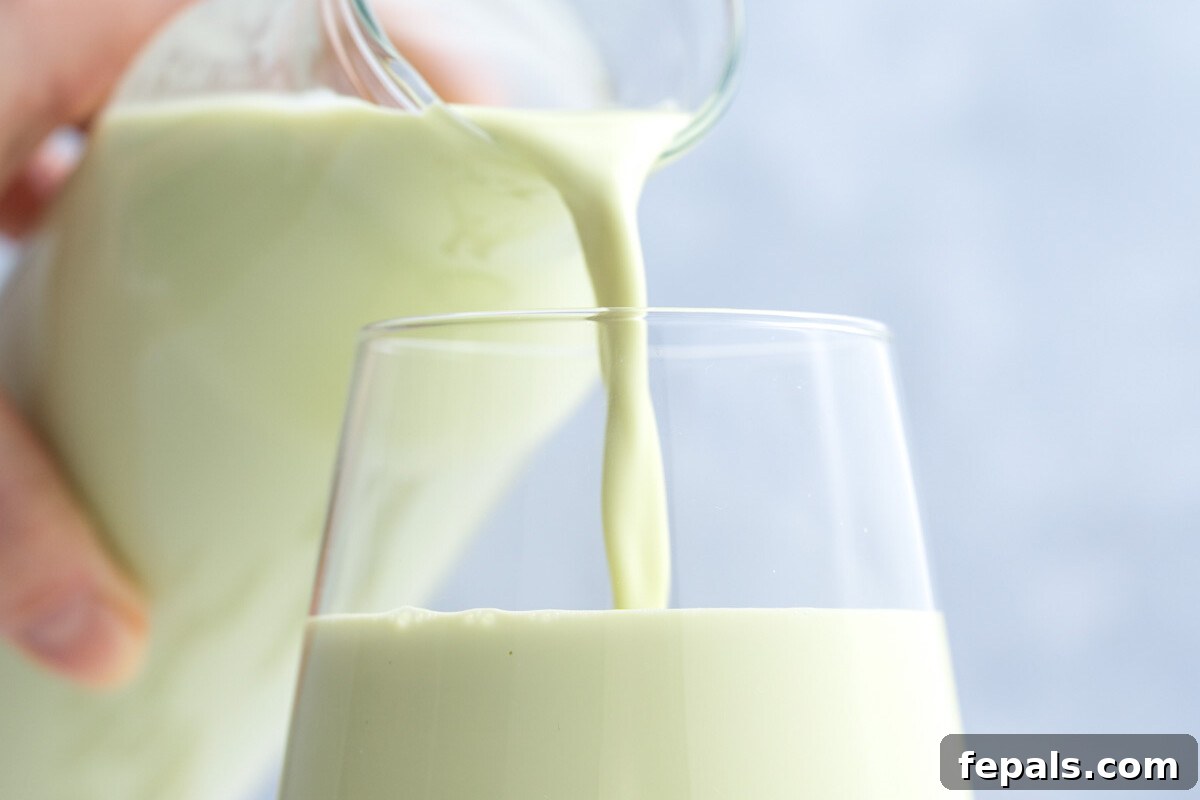 Someone pouring homemade pistachio milk into a glass cup.