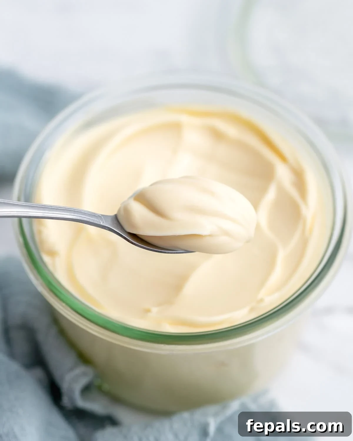 Spoon lifting a generous dollop of creamy homemade mayonnaise from the jar, showing its thick, stable texture as it holds its shape.