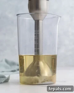 Immersion blender held steady at the bottom of the jar, with the base of the mixture starting to thicken into creamy mayonnaise.