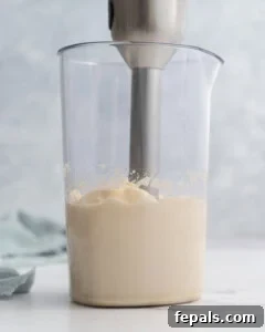Fully blended thick, creamy homemade mayonnaise in a tall glass jar with an immersion blender in it, ready to be transferred.