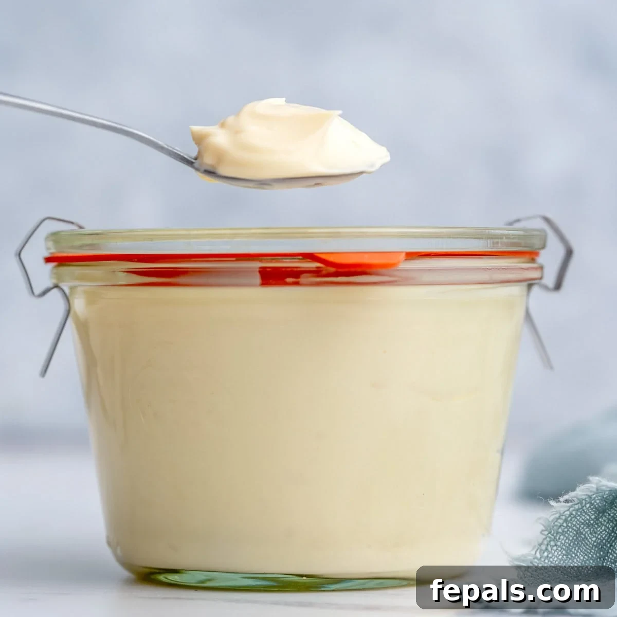 Finished homemade mayonnaise stored in a small glass jar with a red-handled lid, sealed and ready for refrigeration.