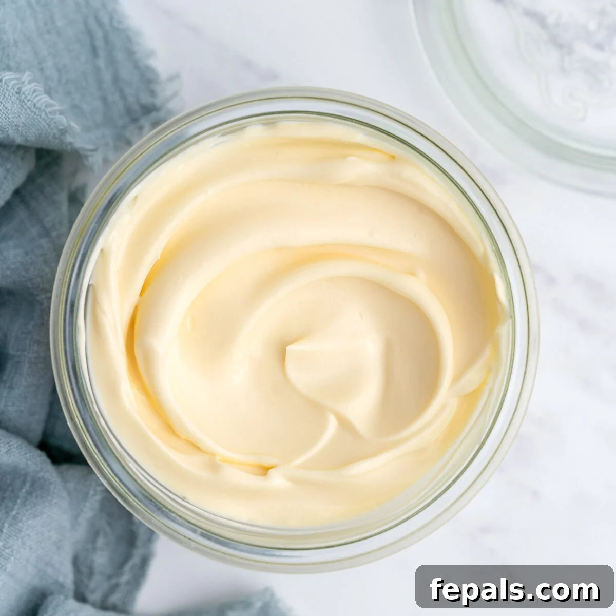 Completed homemade mayonnaise in an open glass jar, showing its glossy, pale yellow surface and creamy texture.
