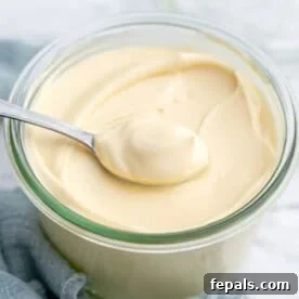 Spoon lifting a generous dollop of creamy homemade mayonnaise from a jar.
