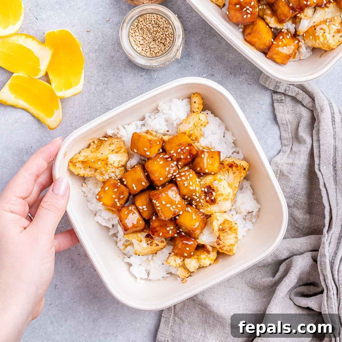 Crispy Orange Tofu 7 A hand holding a meal prep bowl filled with rice and crispy orange tofu, ready to eat.