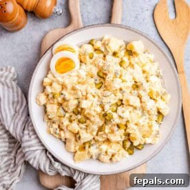 A large white plate with potato salad and a wooden spoon on the side.