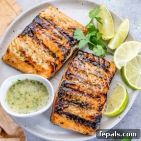 Two succulent grilled salmon fillets on a white plate, garnished with fresh lime wedges and a side of vibrant cilantro lime sauce.