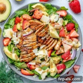 A colorful salad bowl featuring grilled chicken, fresh strawberries, creamy avocado, and crumbled cheese.