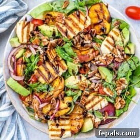 A round, deep plate holding a vibrant salad topped with perfectly grilled halloumi and sweet grilled peaches, drizzled with dressing.