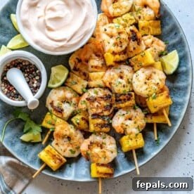 A top-down view of perfectly grilled shrimp skewers with pineapple, served on a vibrant blue plate.