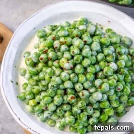 A white bowl filled with richly creamy peas, ready to be served as a comforting side dish.