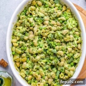 A top-down view of vibrant green mac and cheese, generously served in a white baking dish.