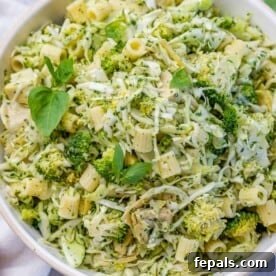 A beautiful green pasta salad, bursting with fresh green vegetables, served in a round white bowl.