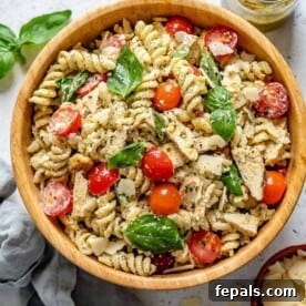 A round bowl brimming with delicious pesto pasta, adorned with colorful tomatoes, tender chicken pieces, and fresh basil garnish.