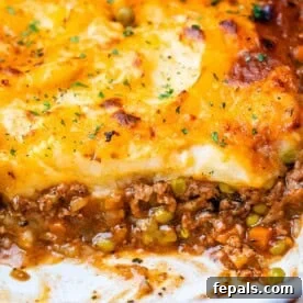 A classic Shepherd's Pie in a white baking dish, showing a rich meat and vegetable filling at the bottom crowned with a golden, creamy mashed potato topping.
