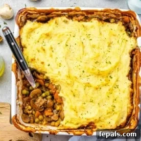 A vegetarian Shepherd's Pie, presented from a top-down view with a spoon scooping out a portion, revealing a rich vegetable filling beneath creamy mashed potatoes.