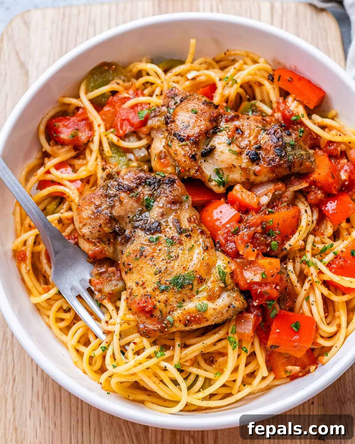 Rustic Hunter's Chicken 7 A white bowl filled with comforting Chicken Cacciatore, served over spaghetti, with a fork ready to enjoy.
