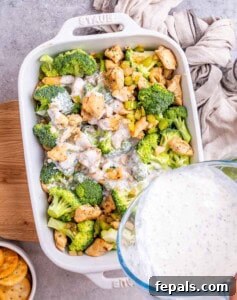 Casserole dish with chicken, broccoli, and sauce topped with cheese, ready for baking.