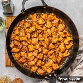 A skillet with chicken bites in a hoisin sauce topped with sesame seeds.